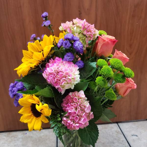 Mixed bouquet in a glass vase with sunflowers, pink roses, and hydrangeas