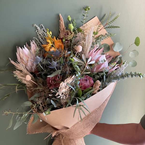 Mixed bouquet with pink protea, orange blooms, and dried grasses wrapped in paper