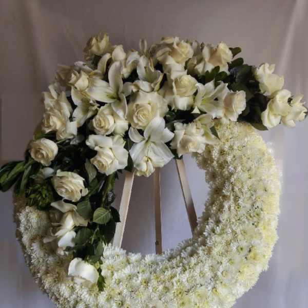 White floral funeral wreath on a stand with roses and lilies