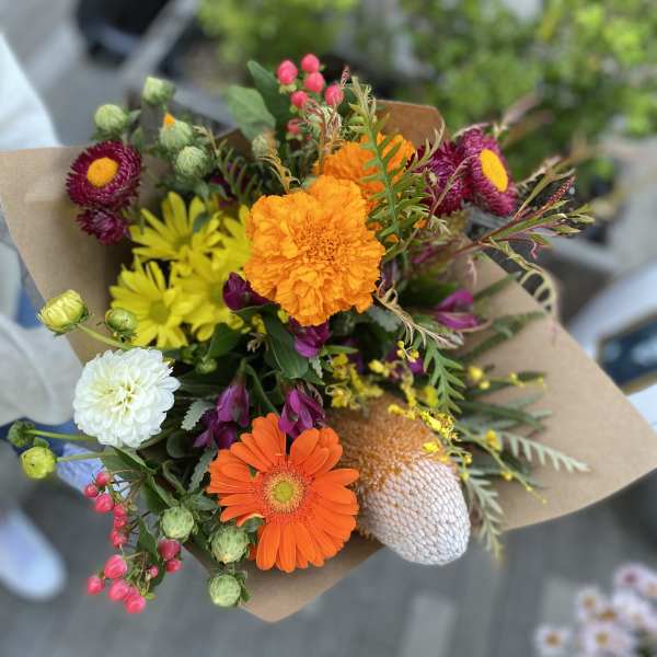 Mixed bouquet with orange, yellow, white, and magenta flowers wrapped in brown paper