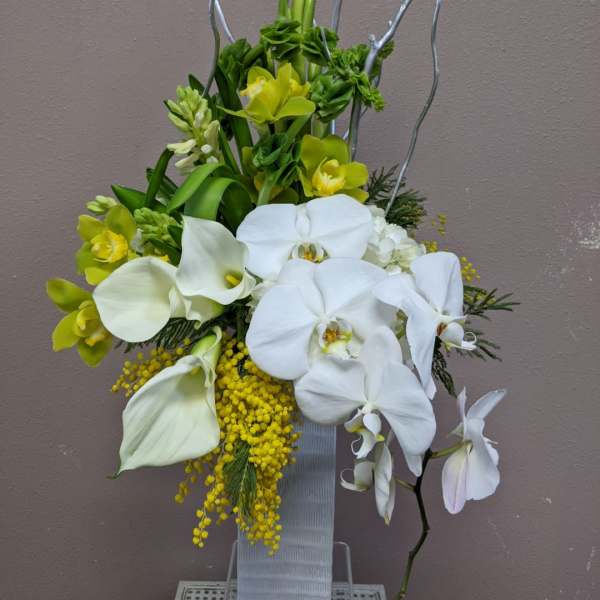 White orchids and calla lilies with yellow accents in a tall vase arrangement