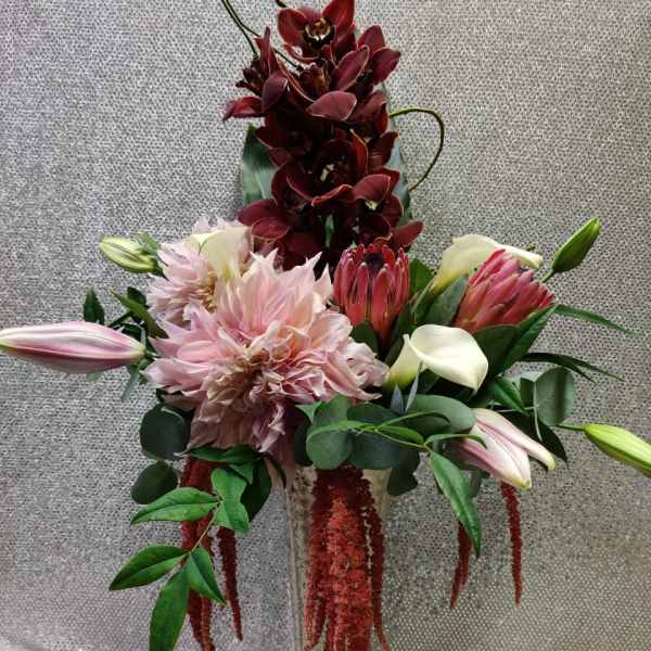 Tall floral arrangement with pink dahlias, burgundy orchids, and lilies in a glass vase