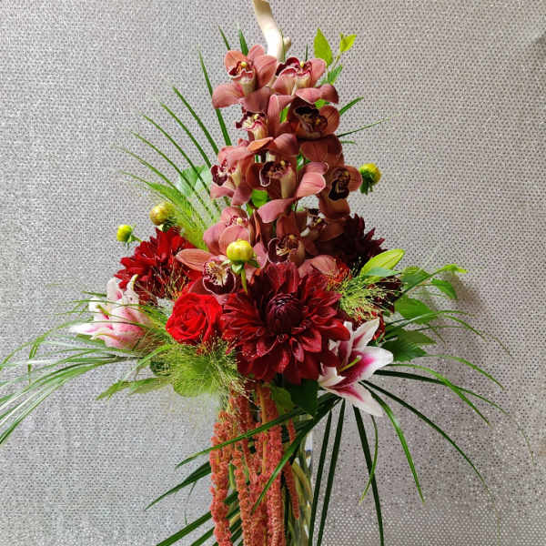 Tall floral arrangement with red and pink blooms in a clear glass vase