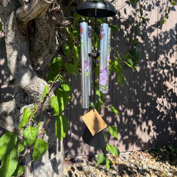 Black wind chime hanging from a tree branch outdoors