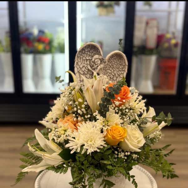 White and peach floral basket with roses, lilies, and an angel figurine.