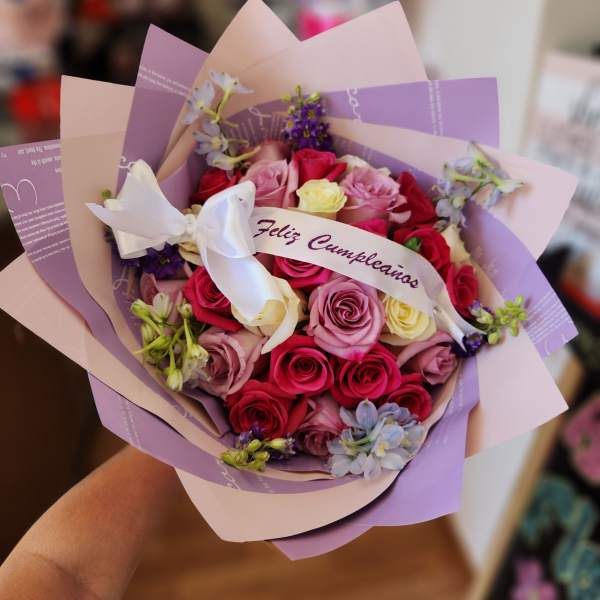 Bouquet of pink, red, and cream roses wrapped in lavender paper with a white ribbon