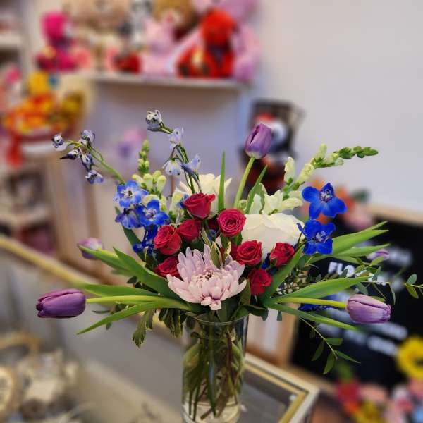 Mixed bouquet of roses, tulips, and blue flowers in a glass vase