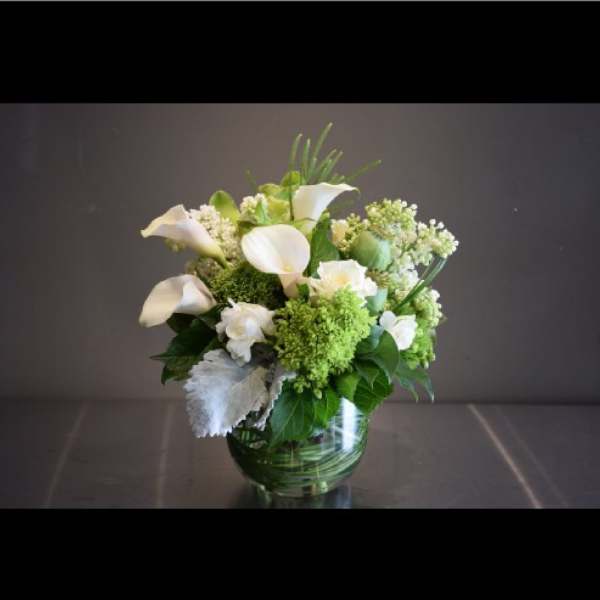 White calla lilies and green-white flowers in a glass vase