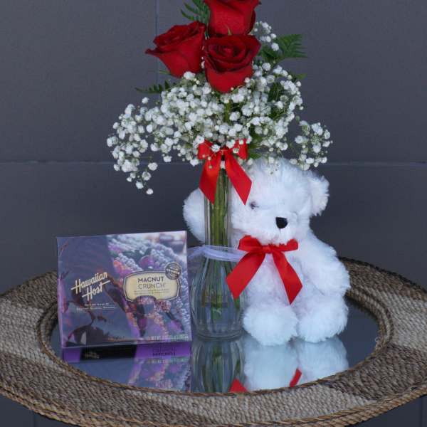 Red roses in a glass vase with a teddy bear and chocolate box