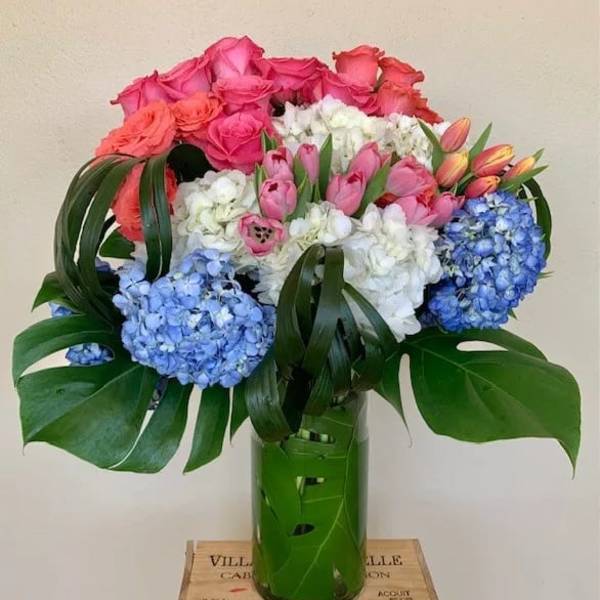 Bouquet of pink roses, tulips, white flowers, and blue hydrangeas in a green vase