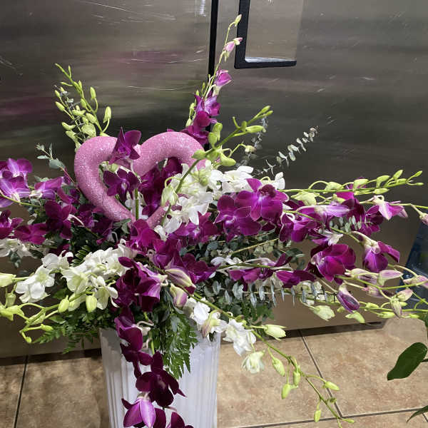 Purple and white orchid arrangement with a pink glitter heart in a white vase