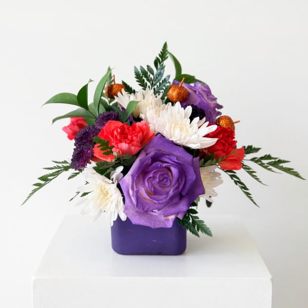 Purple and red floral arrangement in a square vase with small pumpkin picks