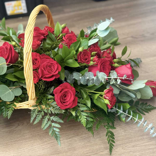 Low wicker basket arrangement of red roses with abundant foliage