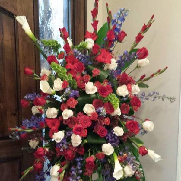 Tall standing spray of red and white roses with purple flowers and white calla lilies on a metal easel.