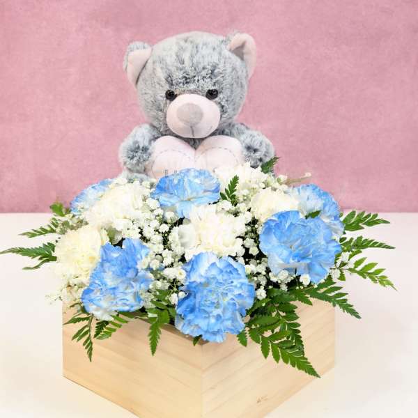 Blue and white carnations in a wooden box with a teddy bear