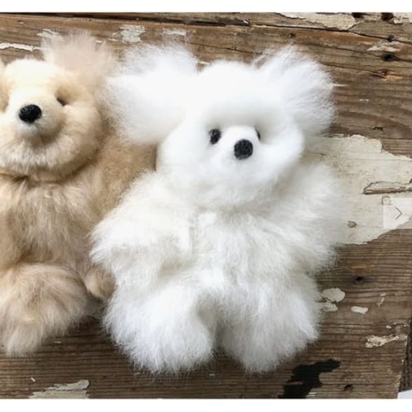 Two fluffy teddy bears, one beige and one white, on a wooden surface.