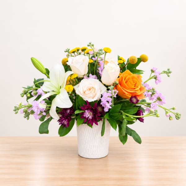 Mixed bouquet of roses, lilies, and purple flowers in a white vase