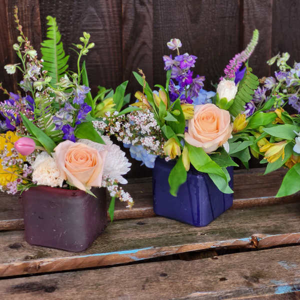 Three mixed floral arrangements in square containers on a wooden surface