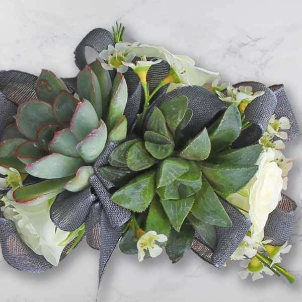 Succulent arrangement with white flowers and dark ribbon on a light surface