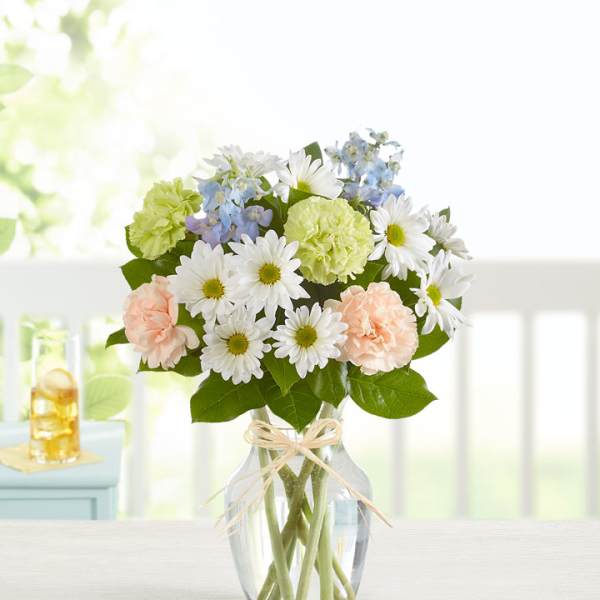 Bouquet of white daisies, pale carnations, and blue flowers in a glass vase