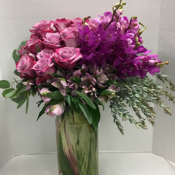 Pink roses and purple orchids arranged in a tall glass vase