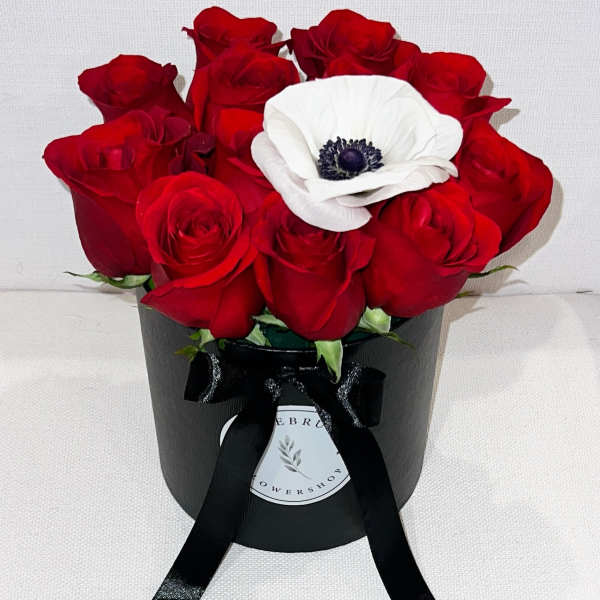 Red roses with a white anemone in a black hatbox tied with ribbon