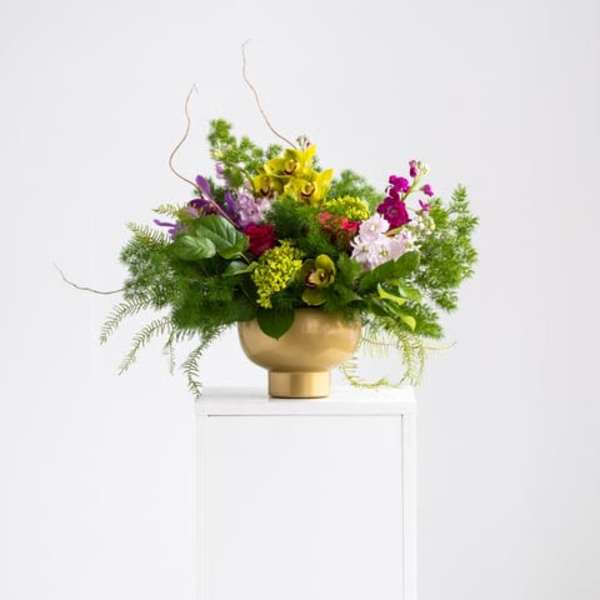 Asymmetrical arrangement of green orchids and mixed bright flowers in a gold pedestal bowl