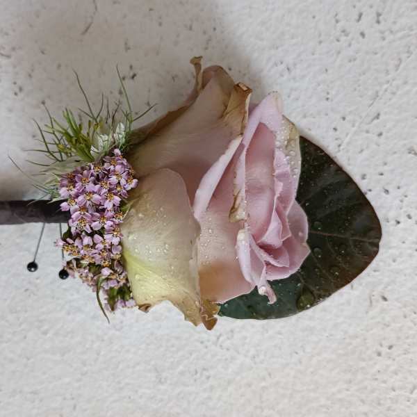 Pink rose boutonniere with small purple filler flowers and a dark leaf