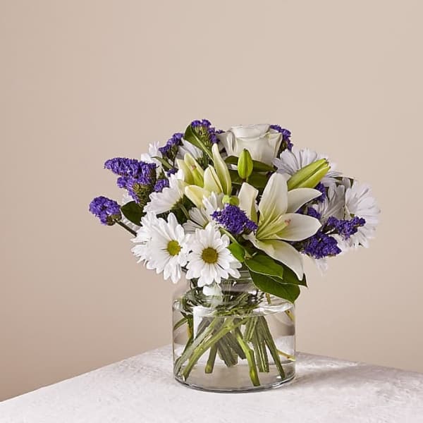 White lilies and daisies in a clear glass vase with purple filler flowers