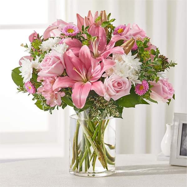 Pink lilies and roses arranged in a clear glass vase