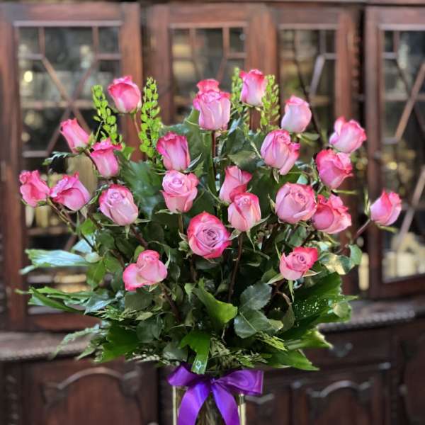 Pink roses arranged in a clear glass vase with a purple ribbon
