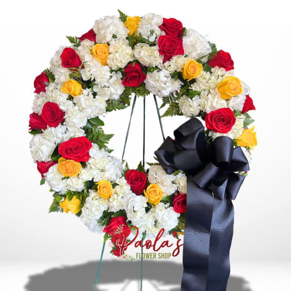Circular wreath of red, yellow, and white flowers with a black ribbon bow