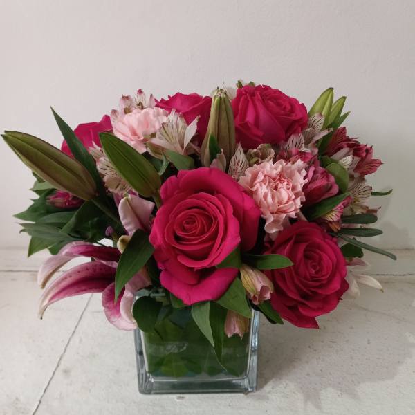 Pink roses and lilies arranged in a square glass vase