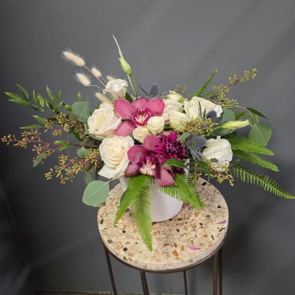 White roses and pink orchids in a white vase with fern foliage