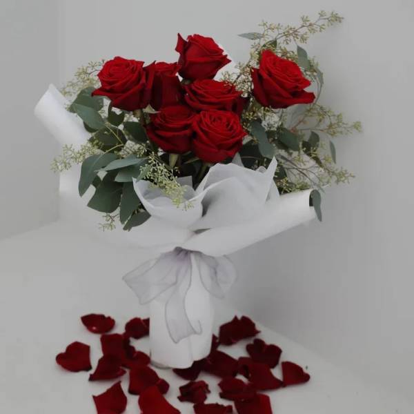 Bouquet of red roses wrapped in white paper with rose petals below