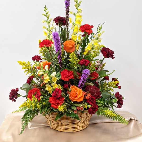 Mixed flower arrangement in a wicker basket with orange roses and red carnations