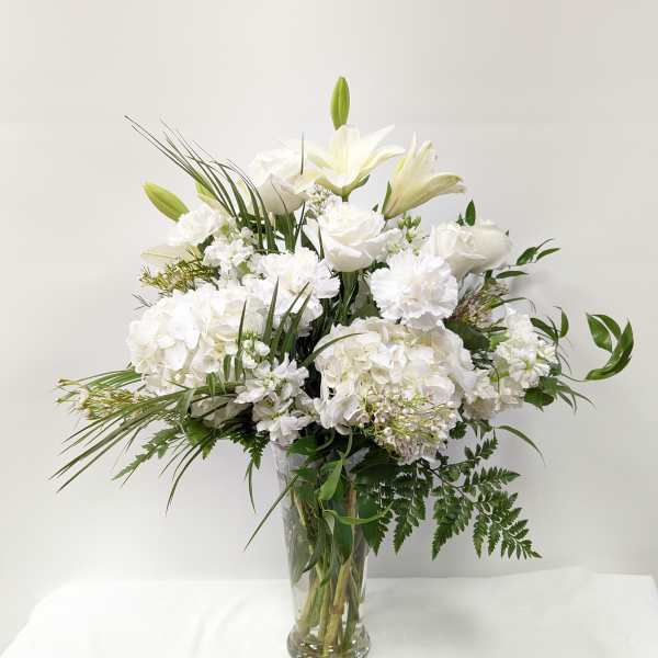 White floral arrangement in a clear glass vase with lilies and roses