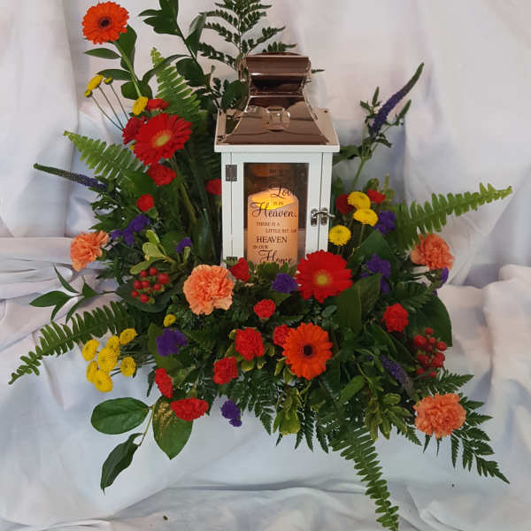 Floral funeral lantern arrangement with mixed bright flowers around a white lantern