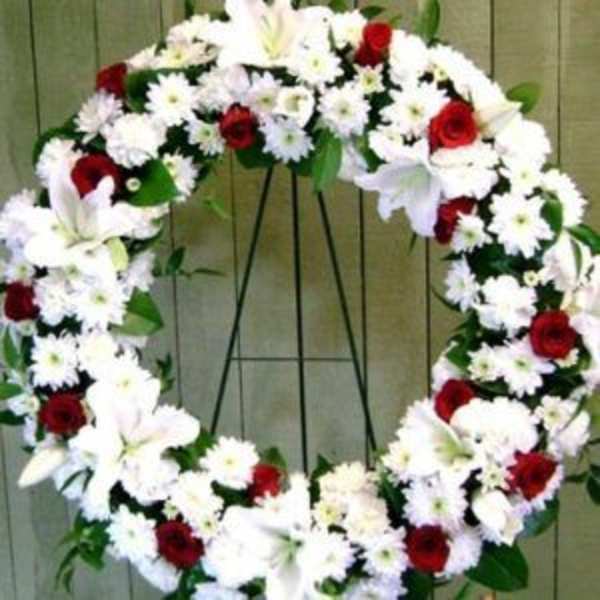 Heart-shaped floral wreath with white flowers and red roses on a stand