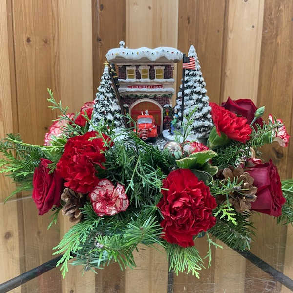 Christmas floral arrangement with red roses and carnations around a small snowy building