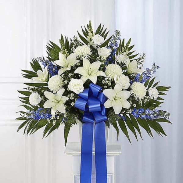 White lilies and blue flowers arranged with a blue ribbon on a stand