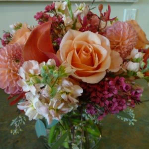 Peach roses and dahlias with pink accent flowers arranged in a clear glass vase