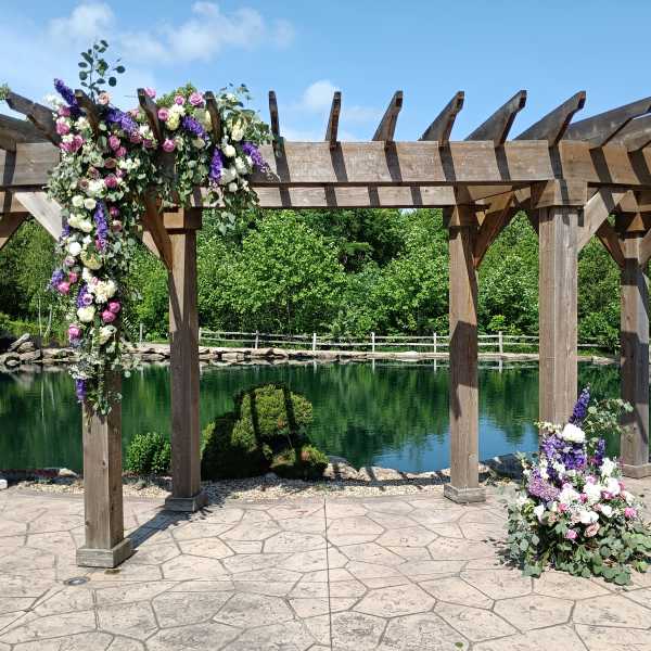 Floral arrangements draped over a wooden pergola beside a pond