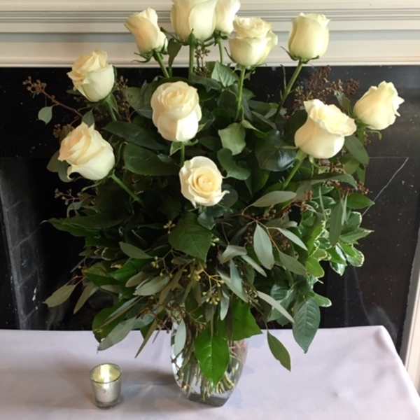 Cream roses arranged in a clear glass vase with greenery.