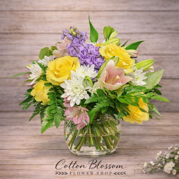 Bouquet of yellow roses, purple blooms, and white daisies in a glass vase