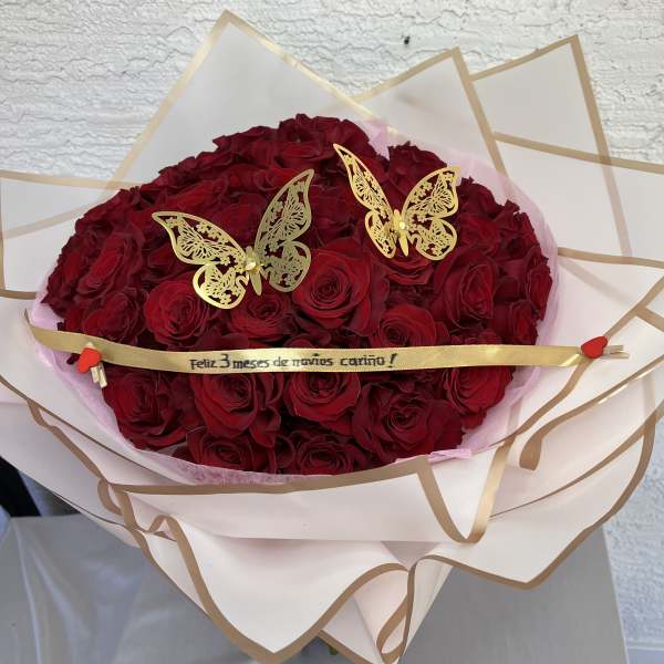 Bouquet of red roses wrapped in cream paper with gold trim and butterfly picks