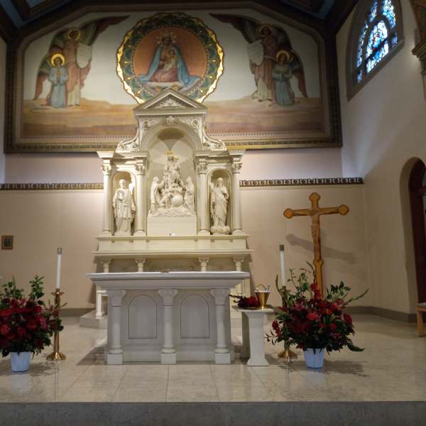 Two red floral arrangements flank a church altar with statues and a crucifix.