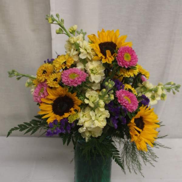 Mixed bouquet with sunflowers, pink daisies, and cream flowers in a green vase