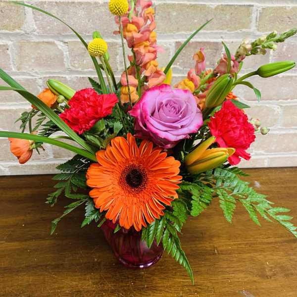 Bright mixed bouquet in a purple glass vase with orange, pink, and red blooms