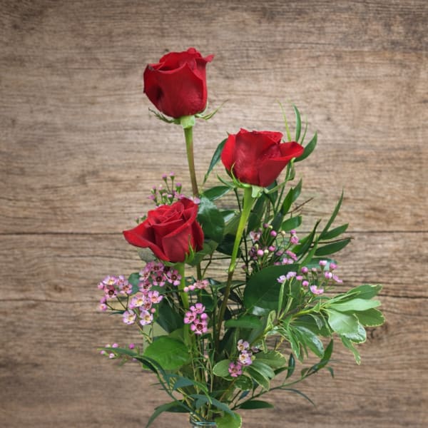 Three red roses in a clear glass vase with pink filler flowers
